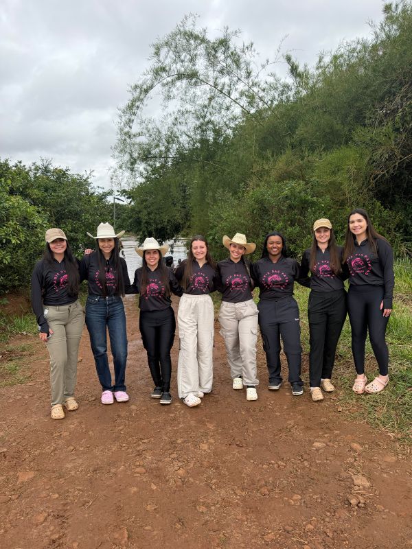 Turma feminina de pesca Patroas da Pesca, com oito mulheres vestindo camisas pretas personalizadas à beira do rio